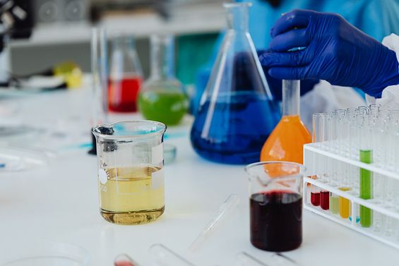 Labortisch mit mehreren chemischen Glasgefäßen, die mit farbigen Flüssigkeiten gefüllt sind.