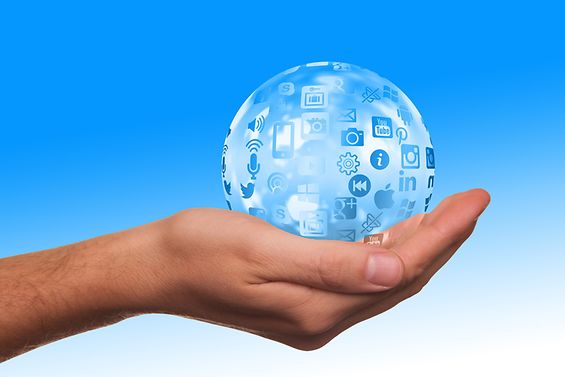 Weltkugel mit Social-Media-Symbolen von Hand gehalten vor blauem Hintergrund
