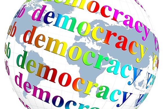 Weltkugel mit Schriftzug "Democracy" in verschiedenen Farben