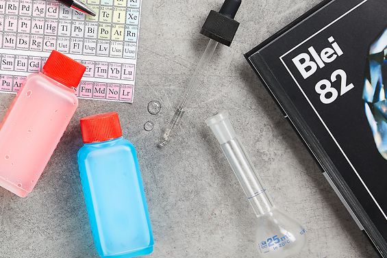 Auf dem Schreibtisch liegt ein Periodensystem, Chemische Substanzen, eine Pipette, ein Glaskolben und ein Buch der Elemente