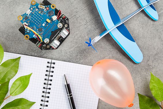 Auf dem Schreibtisch liegt ein Caliope-Minicomputer, ein Spielflugzeug, ein Luftballon, ein Notizbuch und ein Stift.