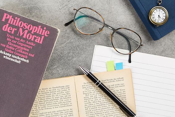 Auf dem Schreibtisch lieben Philosophiebücher, eine Brille, eine kleine Taschenuhr und ein Stift.