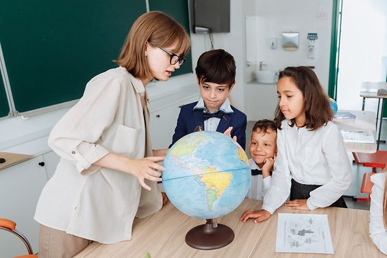 Lehrerin und drei junge Schulkinder um einen Globus