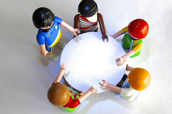 Fünf verschiedene Playmobil-Figuren sitzen an einem runden Tisch
