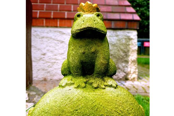 Skulptur von einem Frosch mit Krone, der auf einer Kugel sitzt.