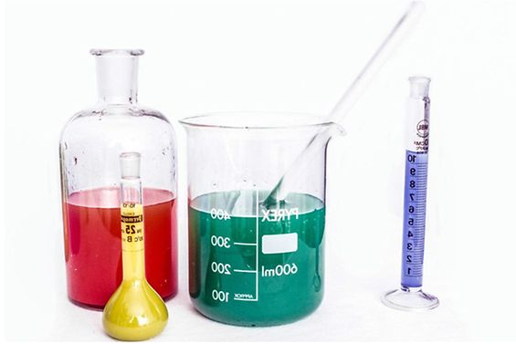 Vier chemische Glasgefäße mit unterschiedlich farbigen Flüssigkeiten gefüllt.