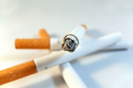 Drei Zigaretten und eine brennende Zigarette auf einem Tisch in Nahaufnahme.