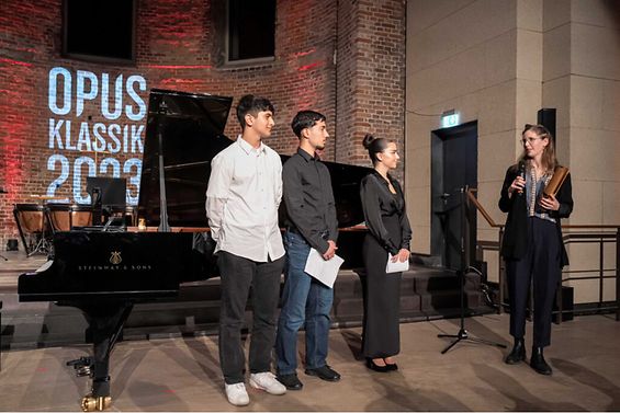 Drei Musiker stehen vor einem Konzert-Flügel daneben eine Moderatorin hält den Opus-Klassik Preis in den Händen.